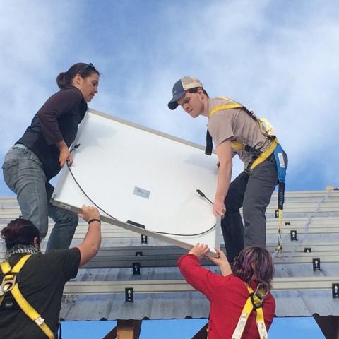 Students lift a solar panel up onto a roof