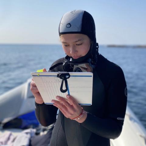 A young woman in a wet suit takes scientific notes